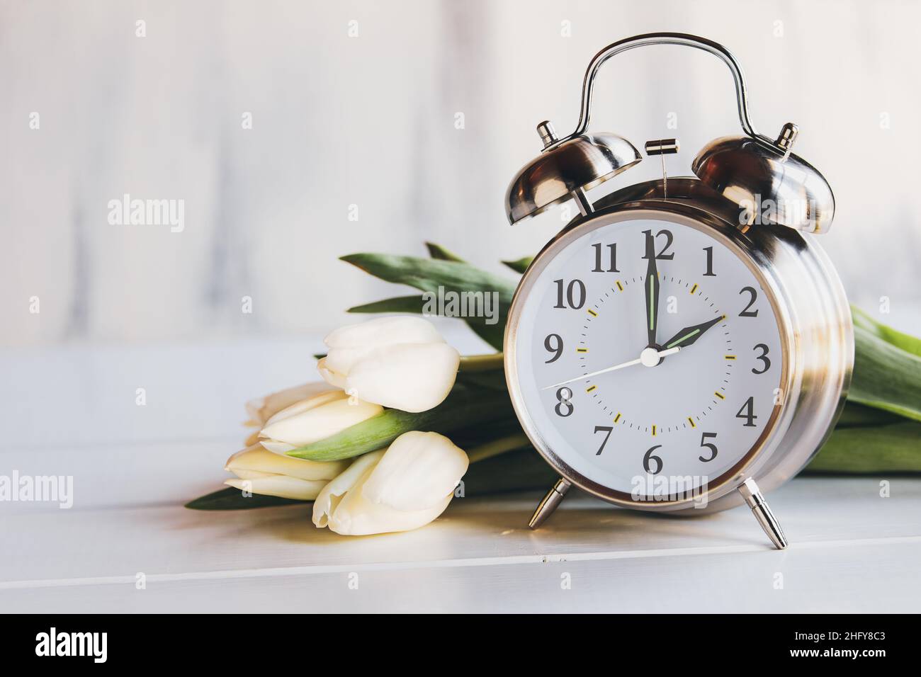 Konzept der Sommerzeit. Stellen Sie Ihre Uhren und auf 2 Uhr mit diesem Bild eines Weckers mit weißen Tulpenblüten ein. Selektiver Fokus Stockfoto