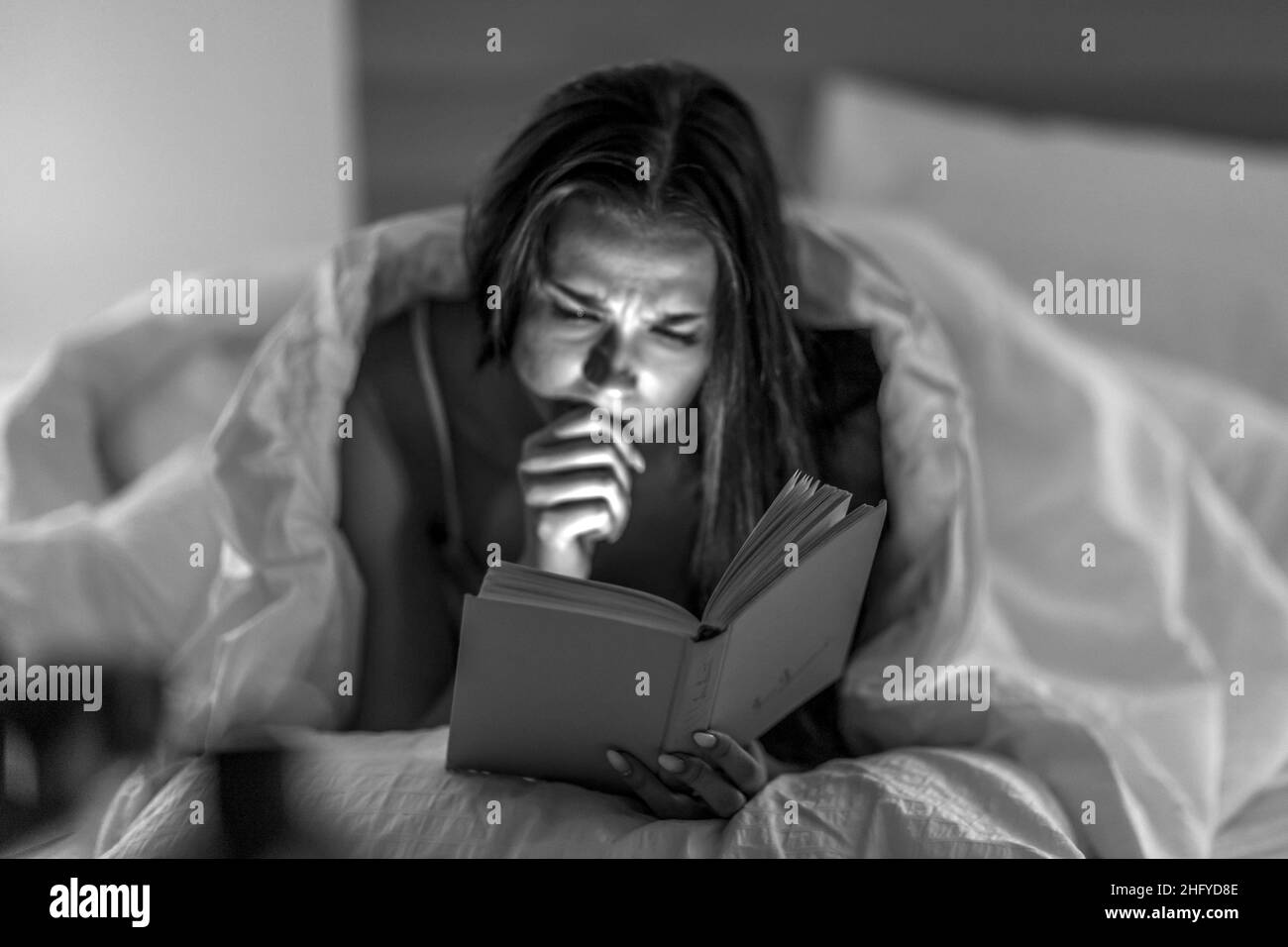 Selbstentwicklung. Entspannung. Literatur. Die schöne Frau liest in ihrem Schlafzimmer vor dem Bett aufmerksam unter schwachem Licht ein Buch. Stockfoto
