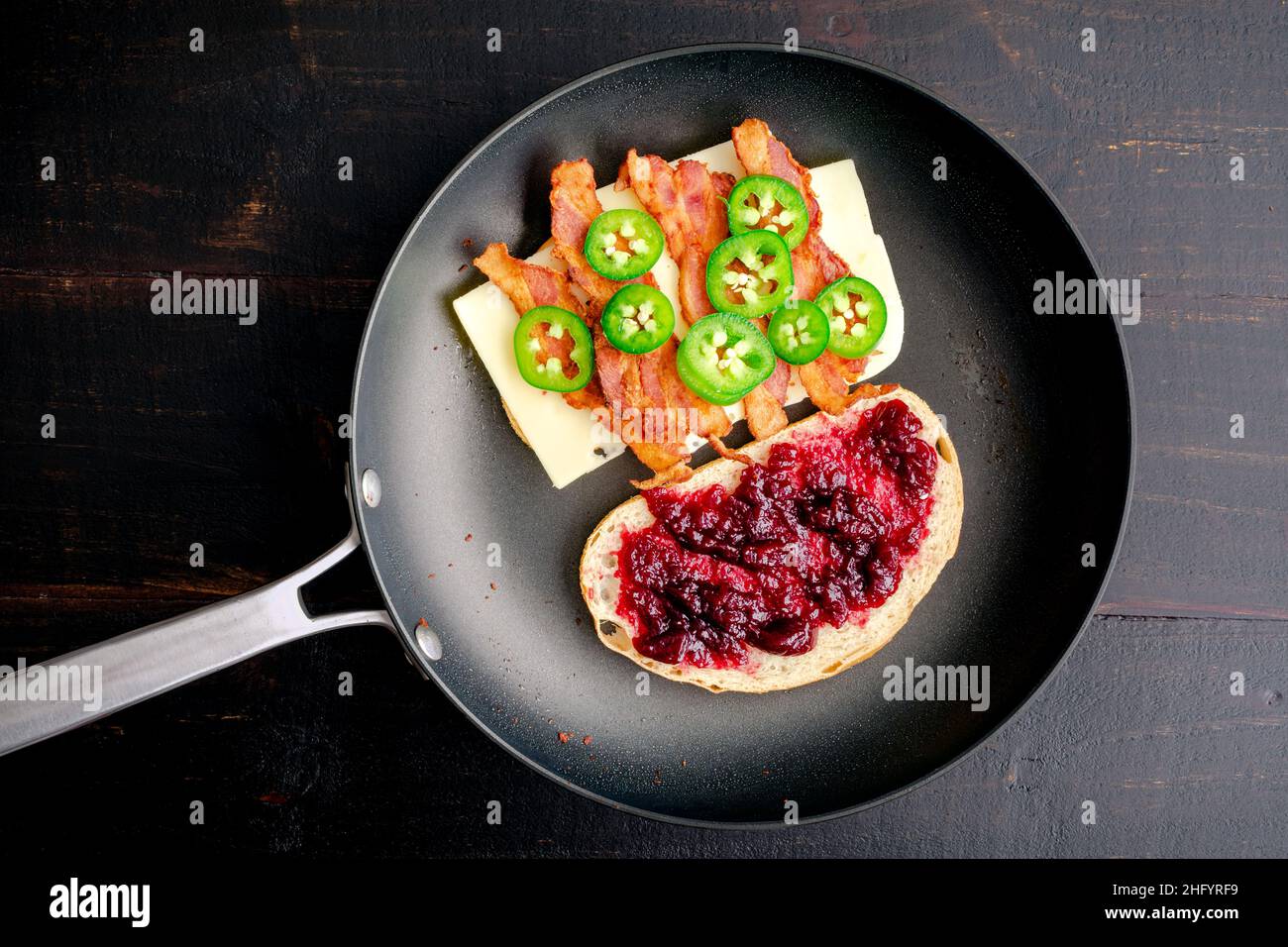 Braten eines Blackberry Bacon Gegrilltes Käse-Sandwich in einer Pfanne: Zwei Hälften eines gegrillten Käse-Sandwiches mit Speck in einer beschichteten Pfanne Stockfoto