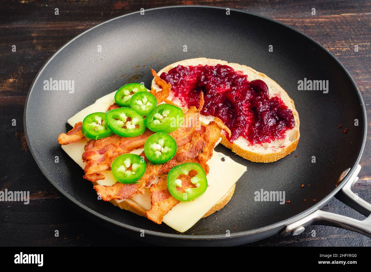 Braten eines Blackberry Bacon Gegrilltes Käse-Sandwich in einer Pfanne: Zwei Hälften eines gegrillten Käse-Sandwiches mit Speck in einer beschichteten Pfanne Stockfoto