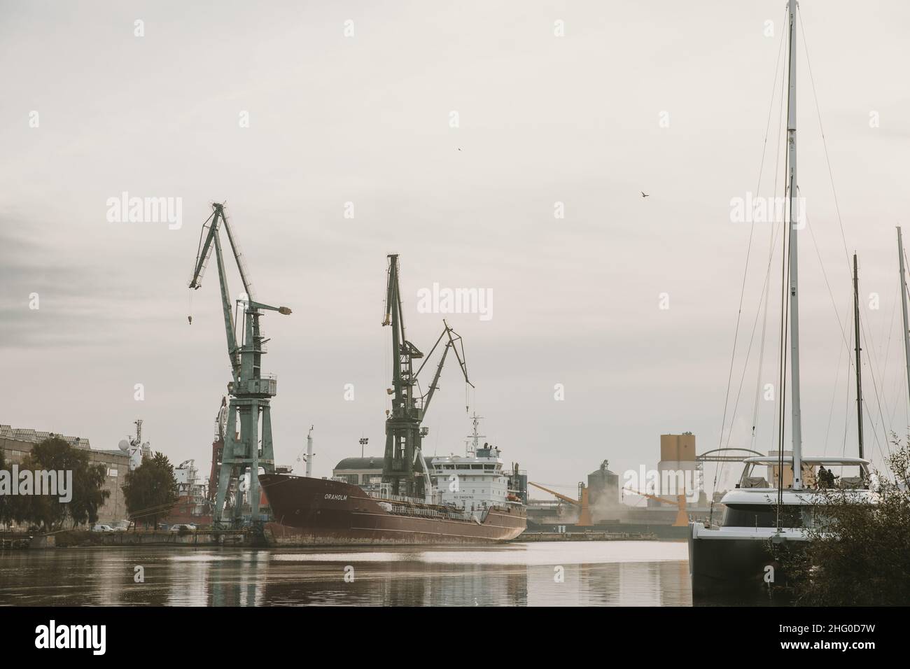 Docks an der Martwa Wisla in der polnischen Stadt Gdańsk mit angedocktem Frachtschiff in Reparatur und Hafenkranen im Hintergrund während des bewölkten Herbstmorgens Stockfoto