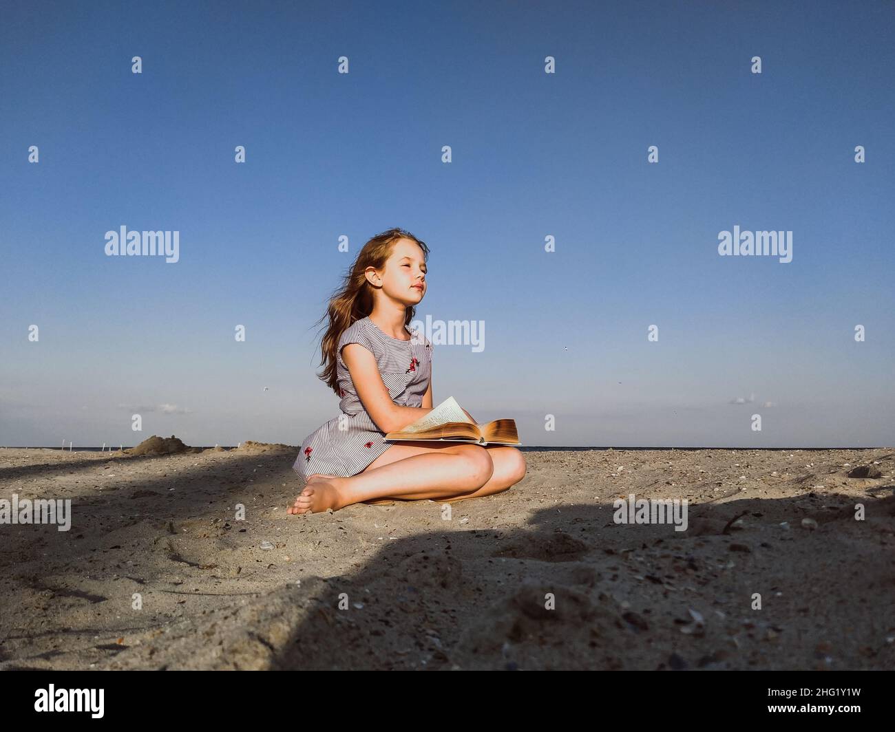 Das kleine Mädchen schaut mit einem Buch am Meer in die Ferne Stockfoto