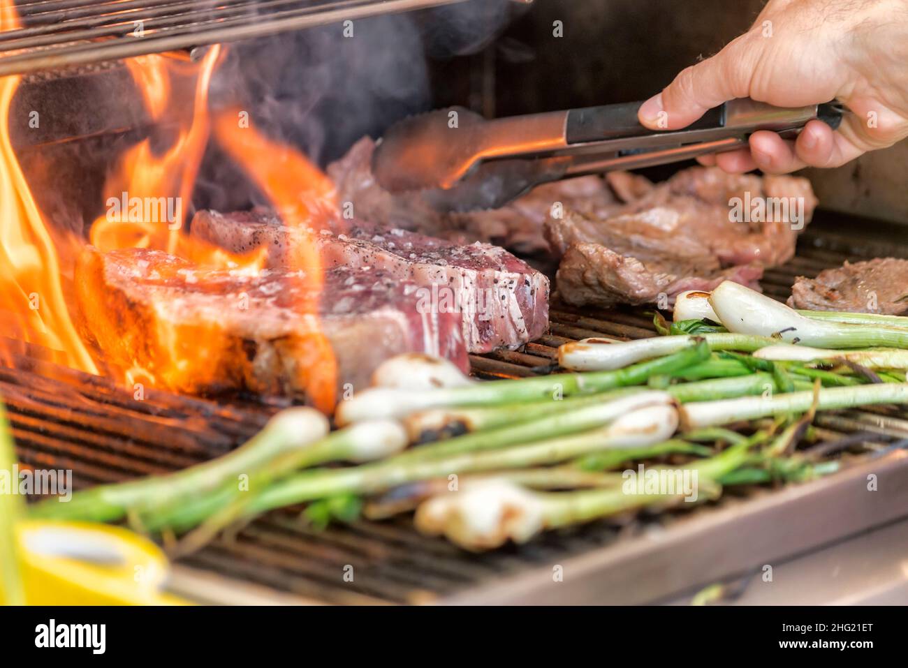 Rohes New York Steak auf dem Grill mit Flammen und Frühlingszwiebeln geröstet Stockfoto