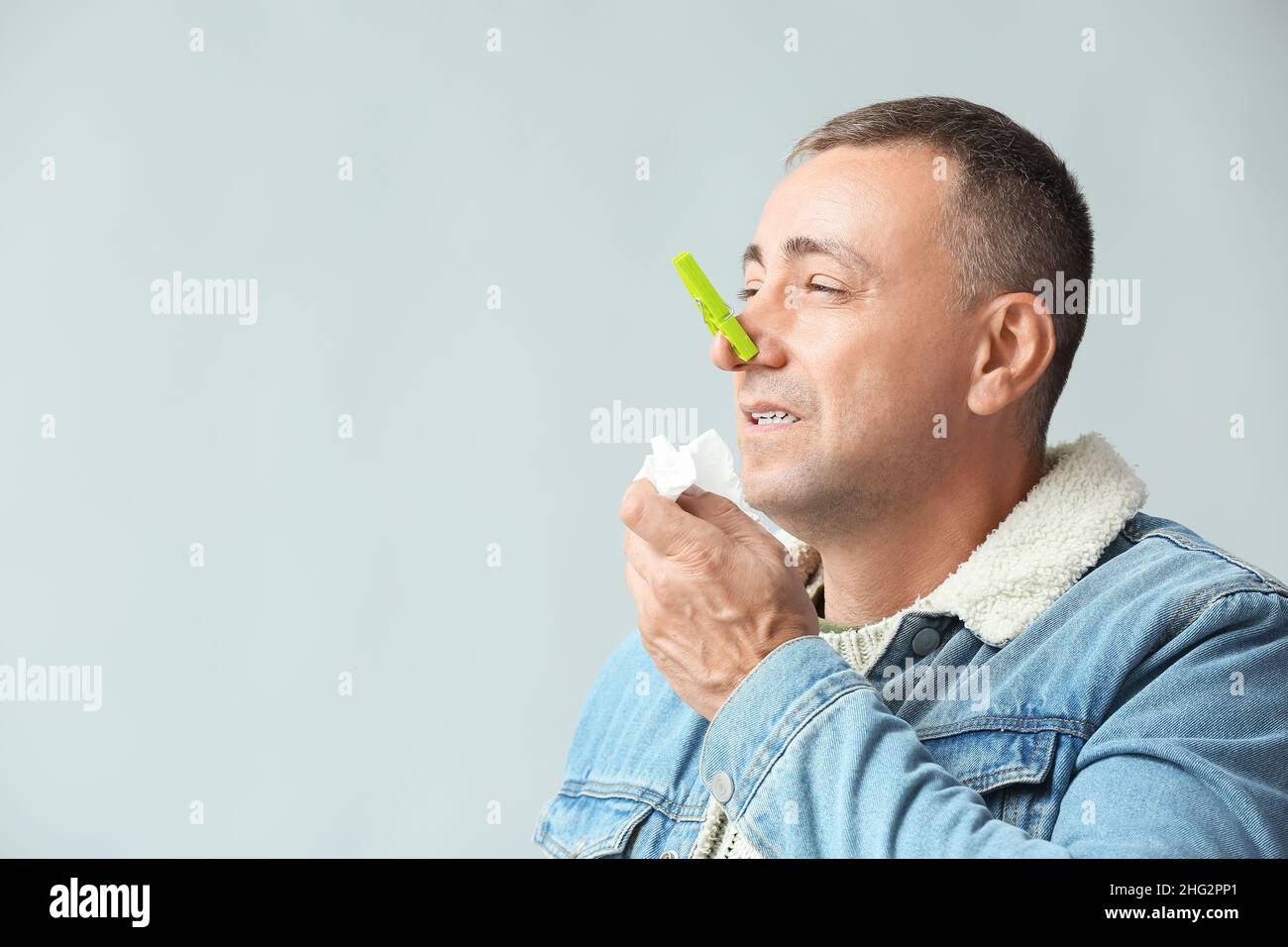 Kranker reifer Mann mit Wäscheklammer auf der Nase vor grauem Hintergrund Stockfoto