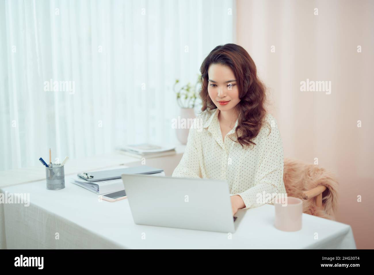 Schöne junge Frau in legerer Kleidung mit Laptop und lächeln Bei der Arbeit in Innenräumen Stockfoto