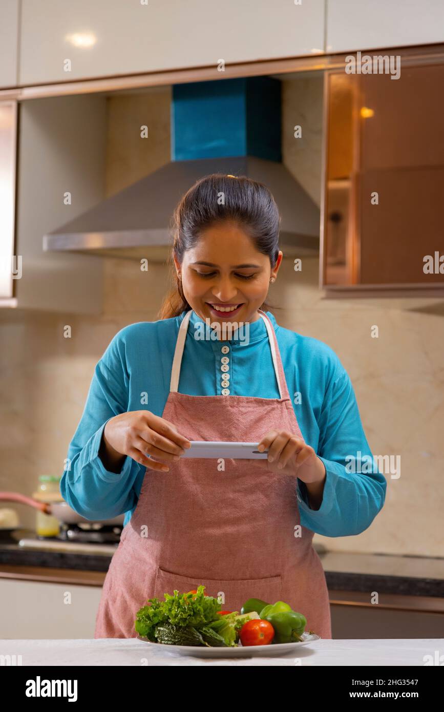 Indische Frau fotografiert Gemüse mit ihrem Handy in der Küche Stockfoto