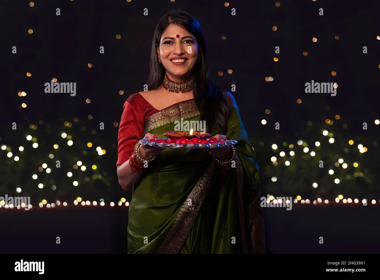 Indische Frau in grünem Saree, die anlässlich von Diwali einen Teller mit Diya hält Stockfoto