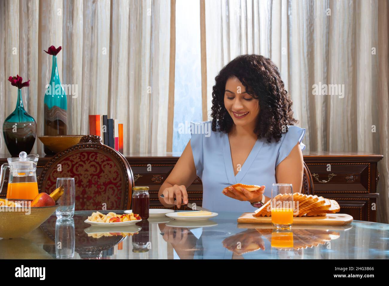 Junge Frau mit lockigen Haaren, die Brot auf dem Tisch schlaff Zu Hause Stockfoto