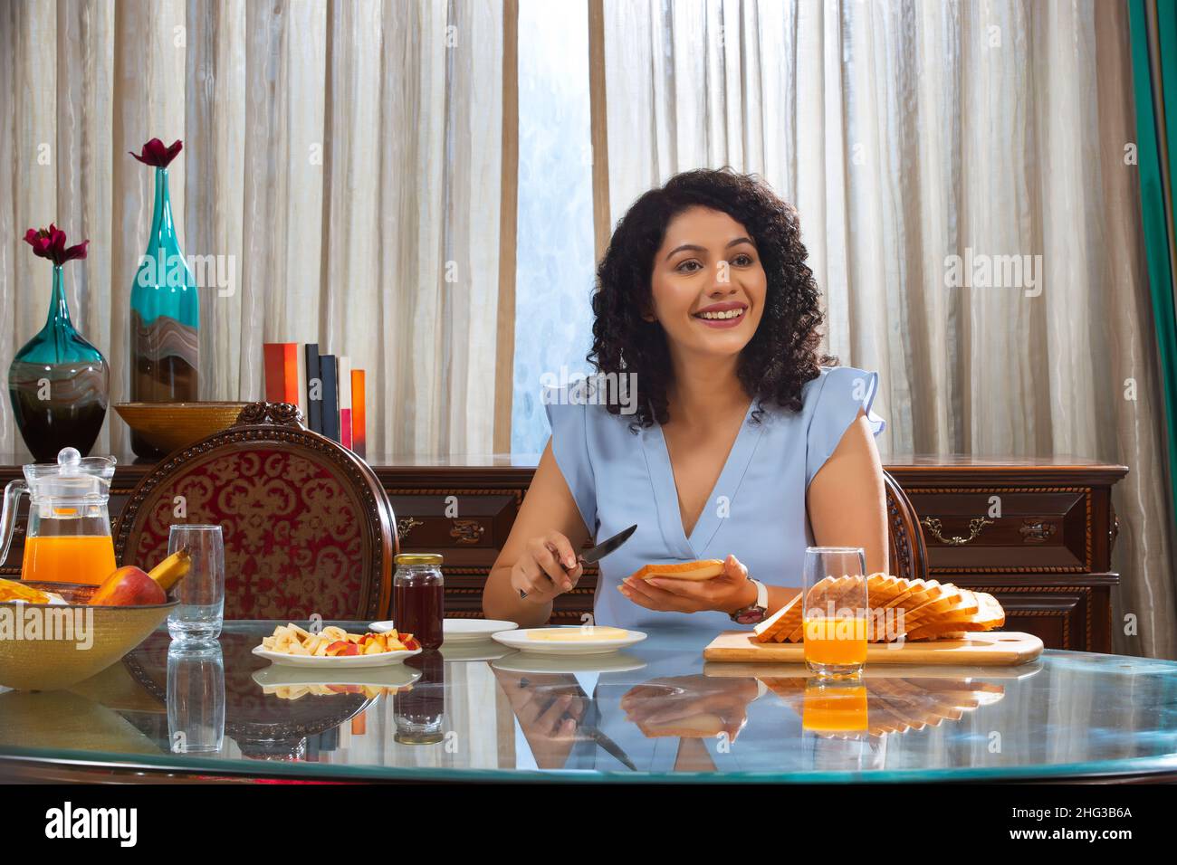 Junge Frau mit lockigen Haaren, die Brot auf dem Tisch schlaff Zu Hause Stockfoto