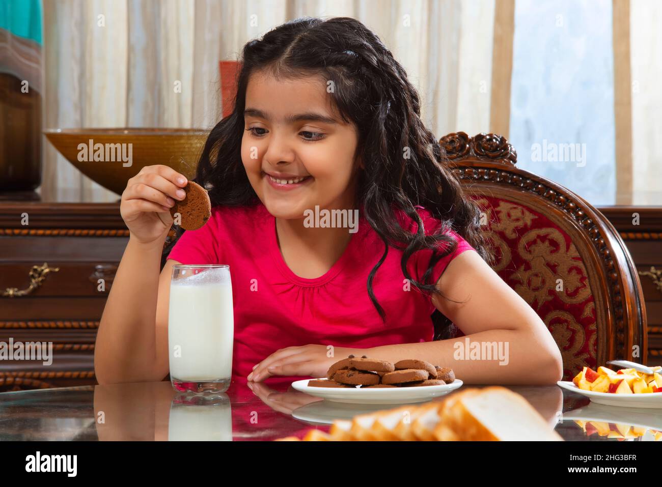 Kleines Mädchen, das während des Frühstücks zu Hause Kekse in Milch eindunkiert Stockfoto