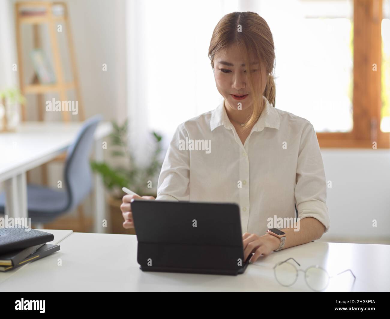 Eine schöne asiatische junge Geschäftsfrau oder Studentin, die an ihrem Arbeitsplatz einen digitalen Tablet-Computer verwendet. Stockfoto