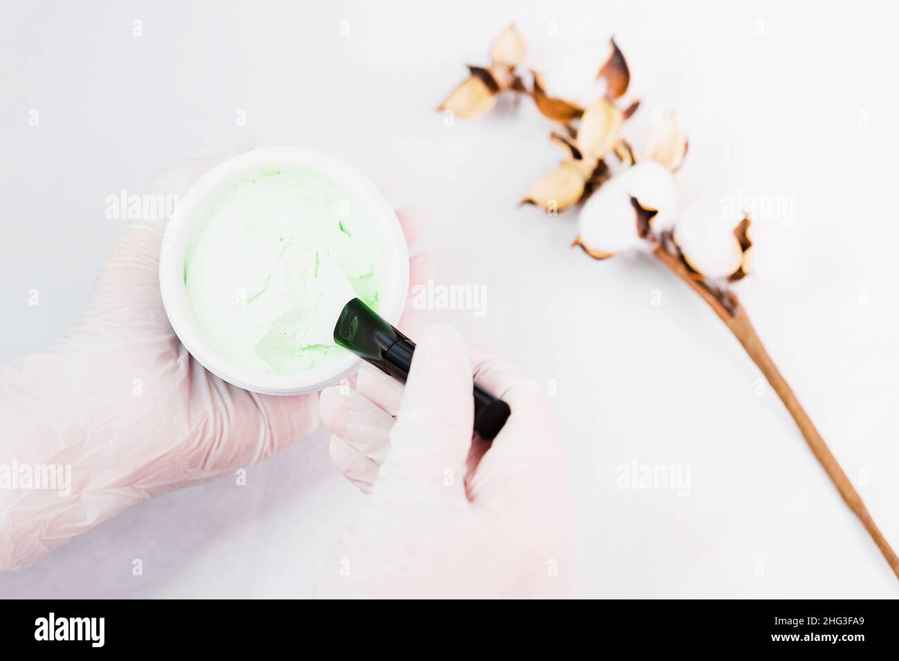 Draufsicht Foto der Kosmetikerin Hände halten einen Darm von Creme für ein Gesicht Haut Verfahren mit einem Baumwollzweig in der Nähe. Stockfoto