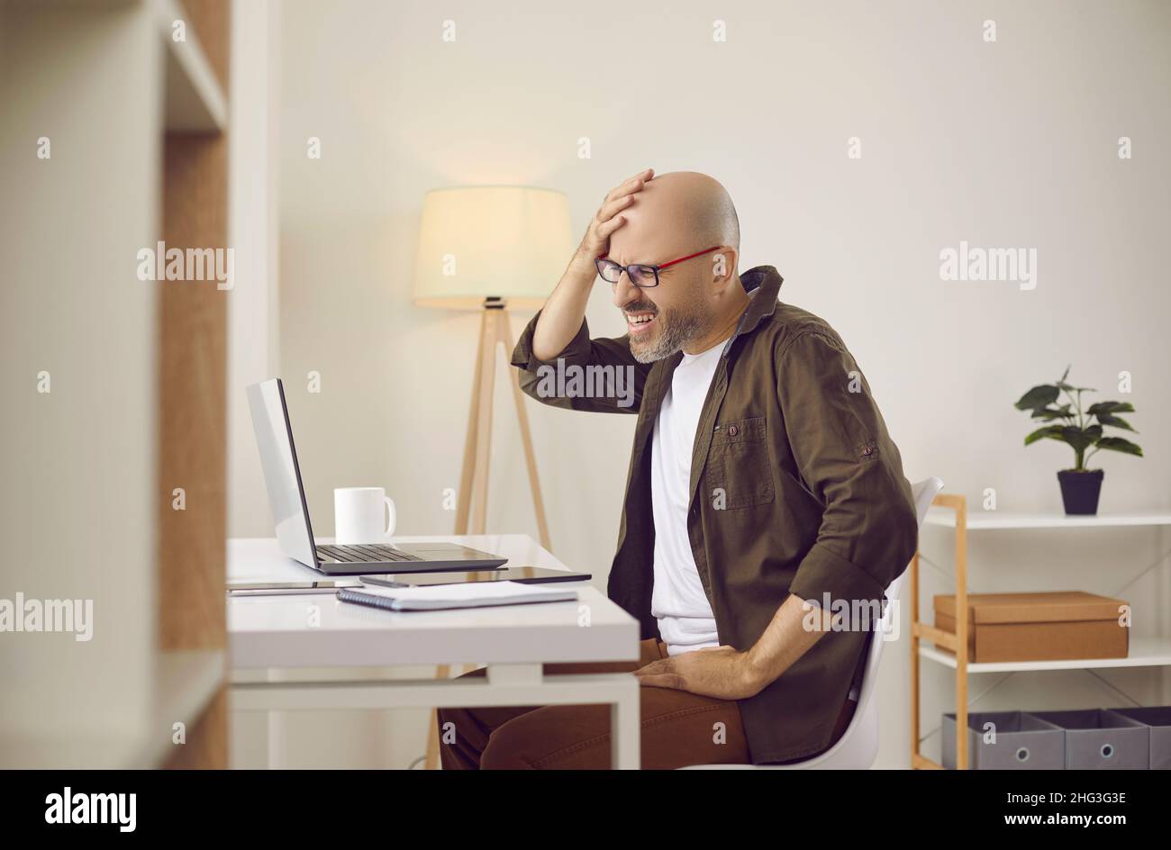 Ein Mann, der beim Arbeiten an einem Laptop Fehler macht oder etwas vergisst, knabscht sich ins Gesicht Stockfoto