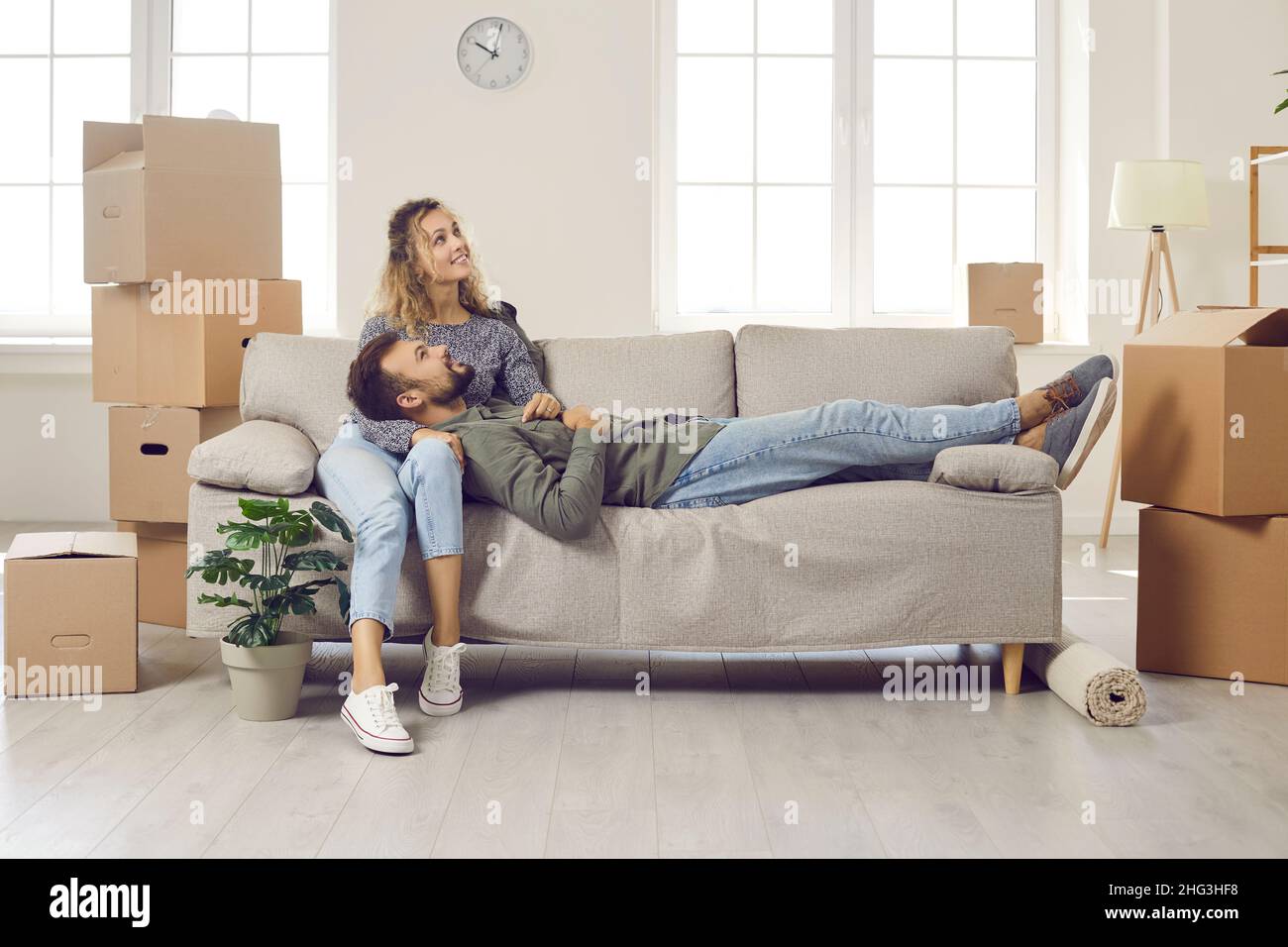 Glückliches junges Paar, das Pause macht und auf dem Sofa sitzt, während es in ihrem neuen Haus umzieht Stockfoto