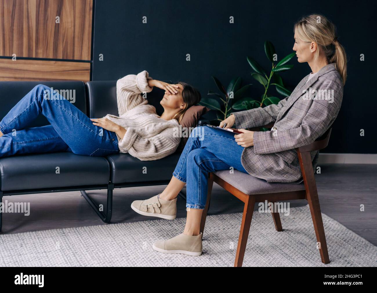 Eine Psychoanalytikerin in einem Workshop hört einer Patientin zu, die auf einer Couch liegt und über ihre Probleme spricht. Stockfoto
