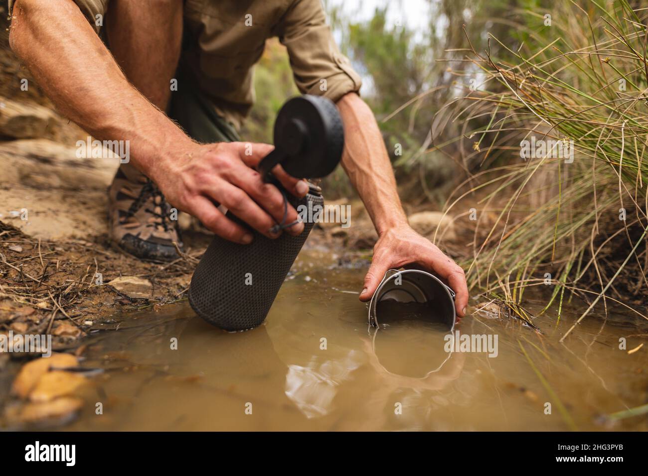 Niedriger Abschnitt des jungen kaukasischen Wanderers, der Wasser in einer Flasche aus einem kleinen Teich sammelt Stockfoto