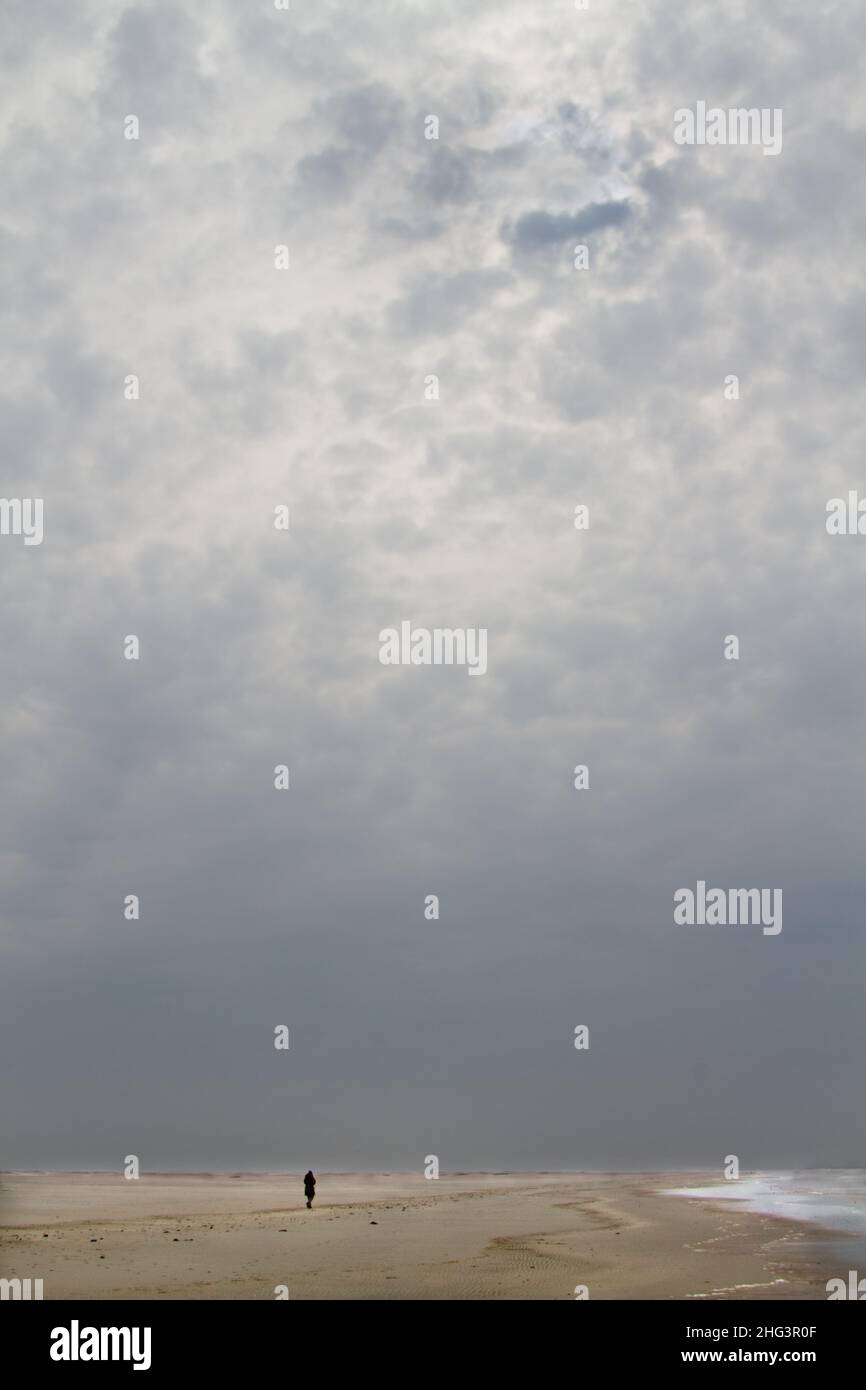 Einsame Person, die am Strand unter einem großen Himmel mit dunklen Wolken läuft Stockfoto