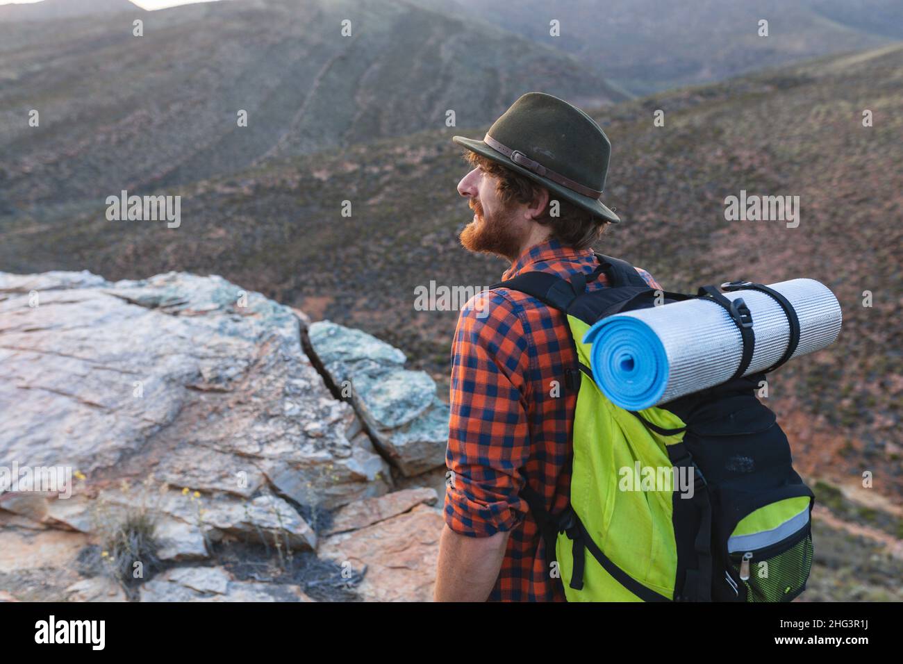 Bärtiger junger kaukasischer Wanderer mit Rucksack und Hut auf dem Berggipfel Stockfoto
