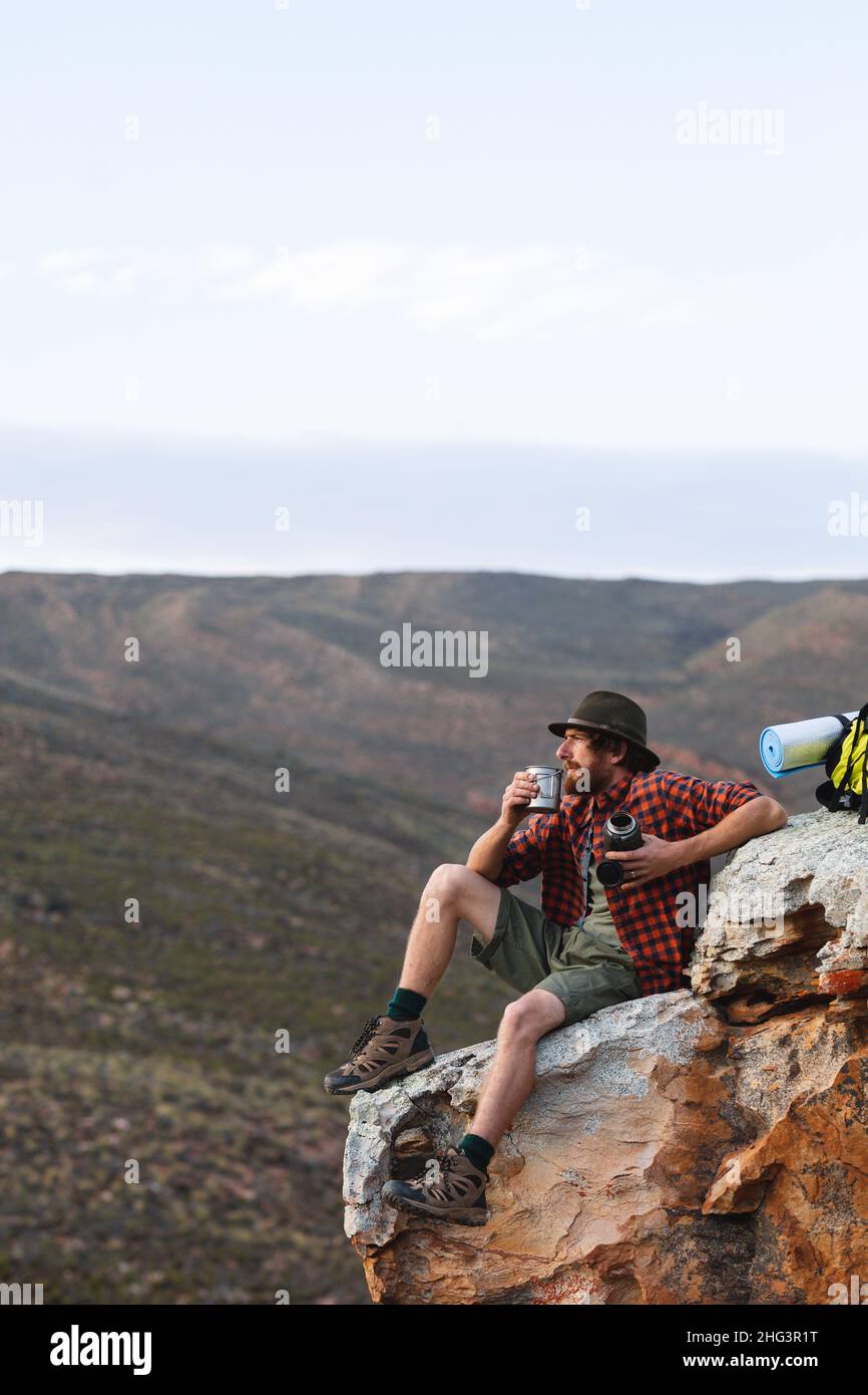 Junger kaukasischer Abenteurer, der mit einem Becher auf einem Felsen auf der Bergspitze sitzt und Platz zum Kopieren hat Stockfoto