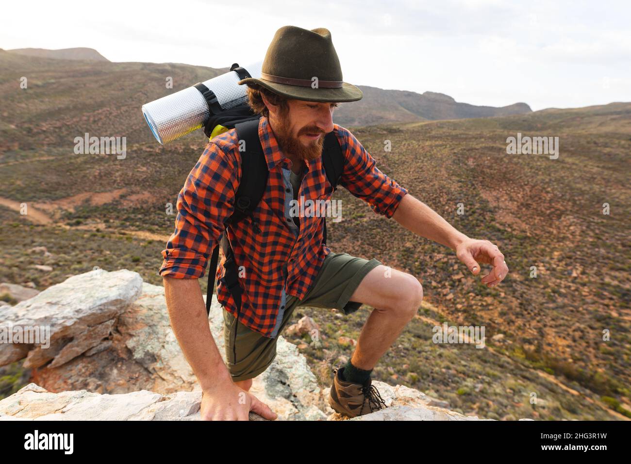 Bärtiger junger kaukasischer Wanderer, der bei Sonnenuntergang den felsigen Berggipfel bestiegen hat Stockfoto