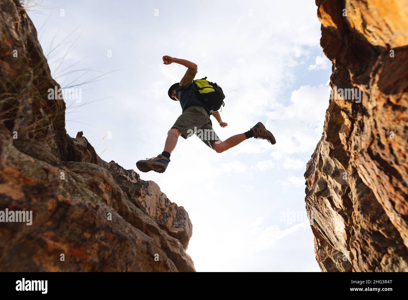 Blick aus der Tiefe auf den energischen kaukasischen Abenteurer mitten in der Luft, während er von einer felsigen Klippe springt Stockfoto
