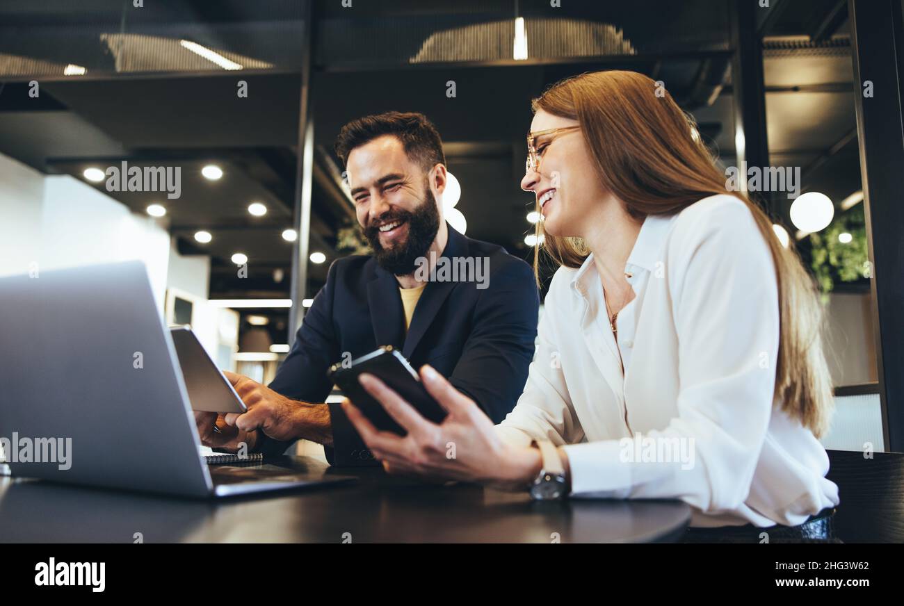 Lächelnde Unternehmer, die drahtlose Technologie nutzen, während sie in einem Büro zusammenarbeiten. Zwei glückliche Geschäftsleute, die sich während des Sitzes ein digitales Tablet angeschaut haben Stockfoto