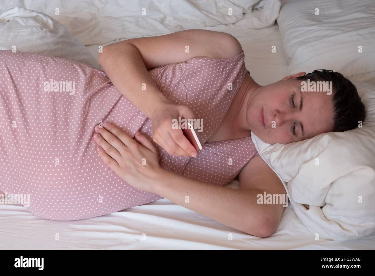 Kaukasische Frau mit Telefon, die zu Hause auf dem Sofa Wehen hat und atmet Stockfoto