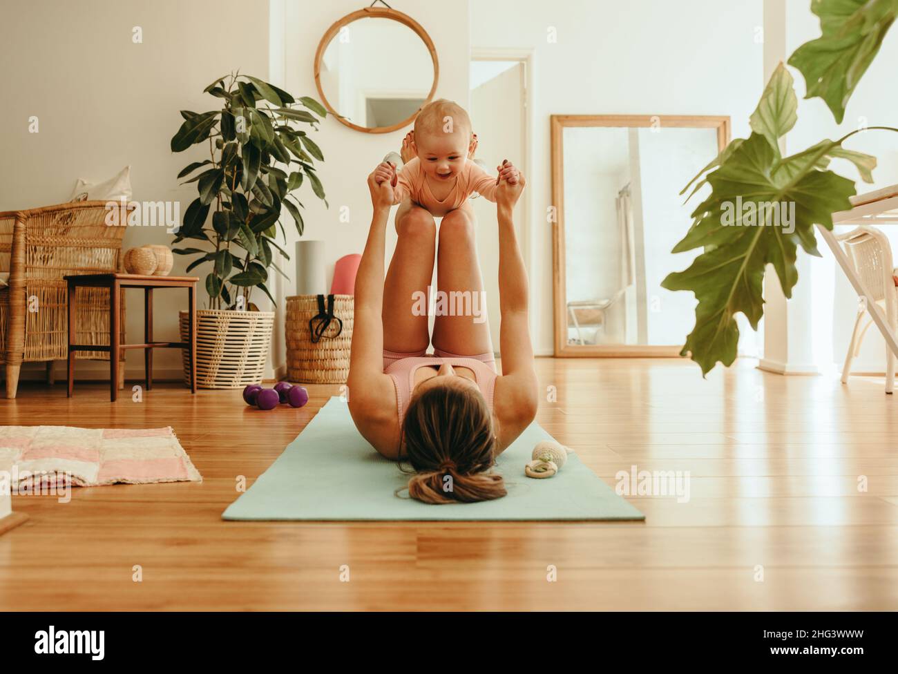 Yogi Mama hebt ihr entzückendes Baby mit ihren Beinen. Gesunde Mutter, die mit ihrem Baby auf einer Trainingsmatte trainiert. Neue Mutter bonding mit ihrem Baby während sie p Stockfoto