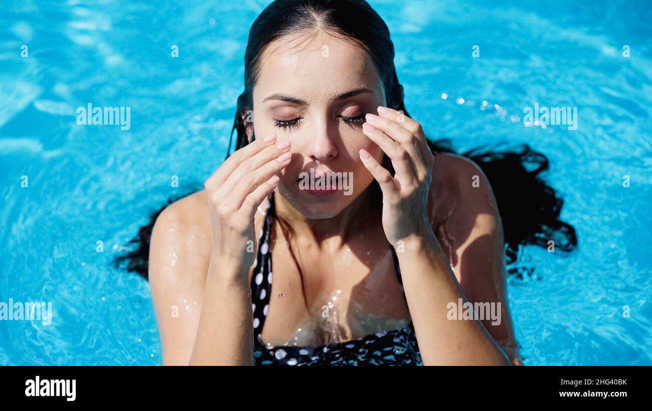 Nasse und brünette Frau mit geschlossenen Augen schwimmend im Pool mit blauem Wasser Stockfoto