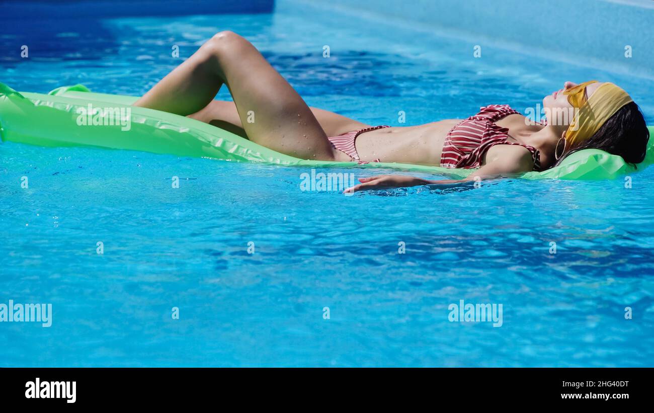 Junge Frau in Sonnenbrillen, die im Schwimmbad auf dem Schwimm-Schwimmer liegt Stockfoto