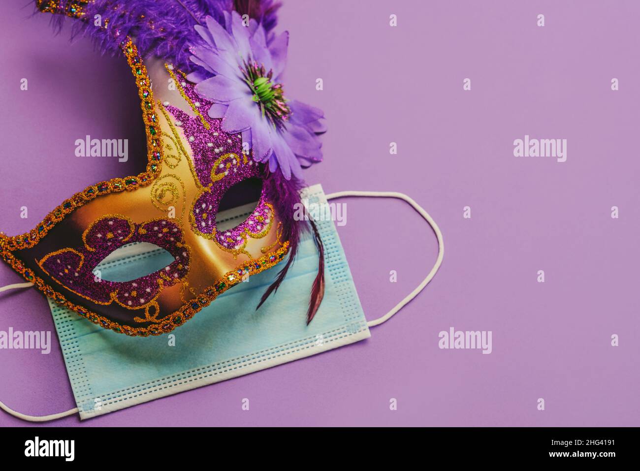 Konzept des Karnevals während des Covid-19. Venezianische Karnevalsmaske mit schützender OP-Maske auf violettem Hintergrund. Konzept der Karnevalsfeier Stockfoto