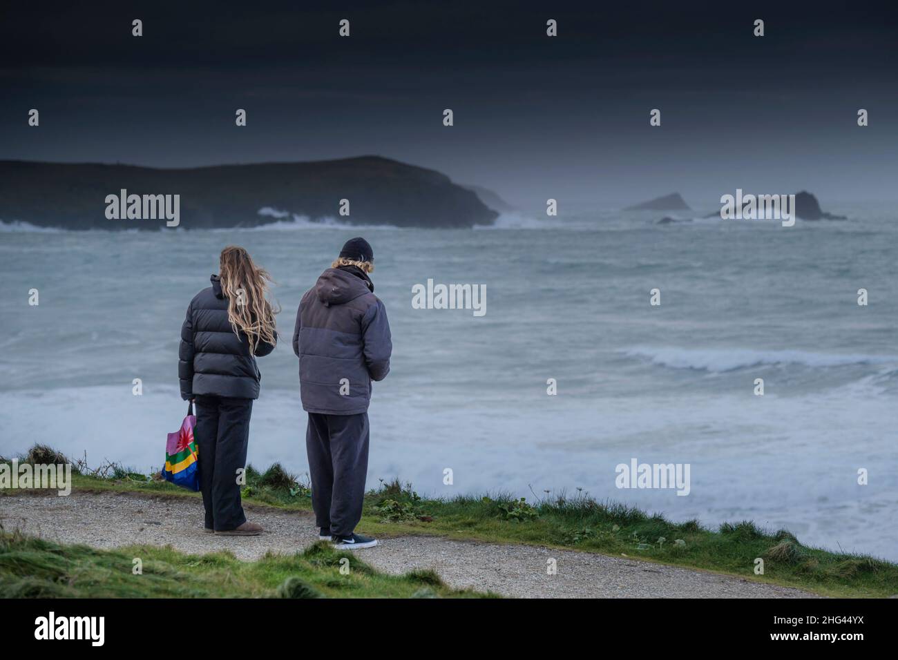 Ein Paar, das bei wildem Winterwetter am Küstenpfad an der Küste von Newquay in Cornwall steht. Stockfoto