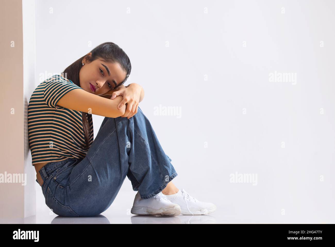 Ein unglückliches junges Mädchen sitzt und lehnt ihren Kopf auf das Knie Stockfoto