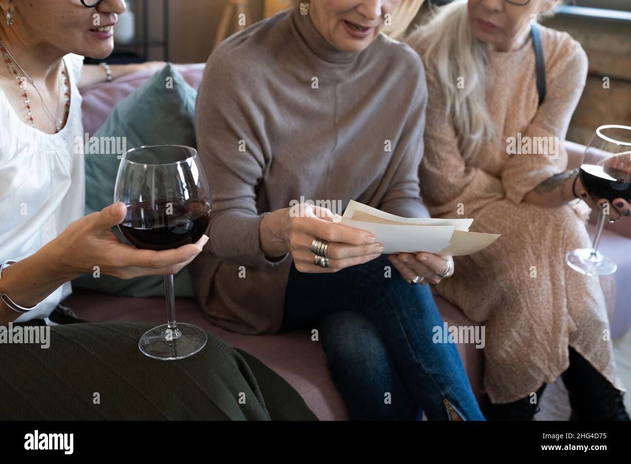 Nahaufnahme einer reifen Frau, die mit ihren Freunden auf dem Sofa sitzt und Fotos ansieht, während sie Rotwein trinkt Stockfoto