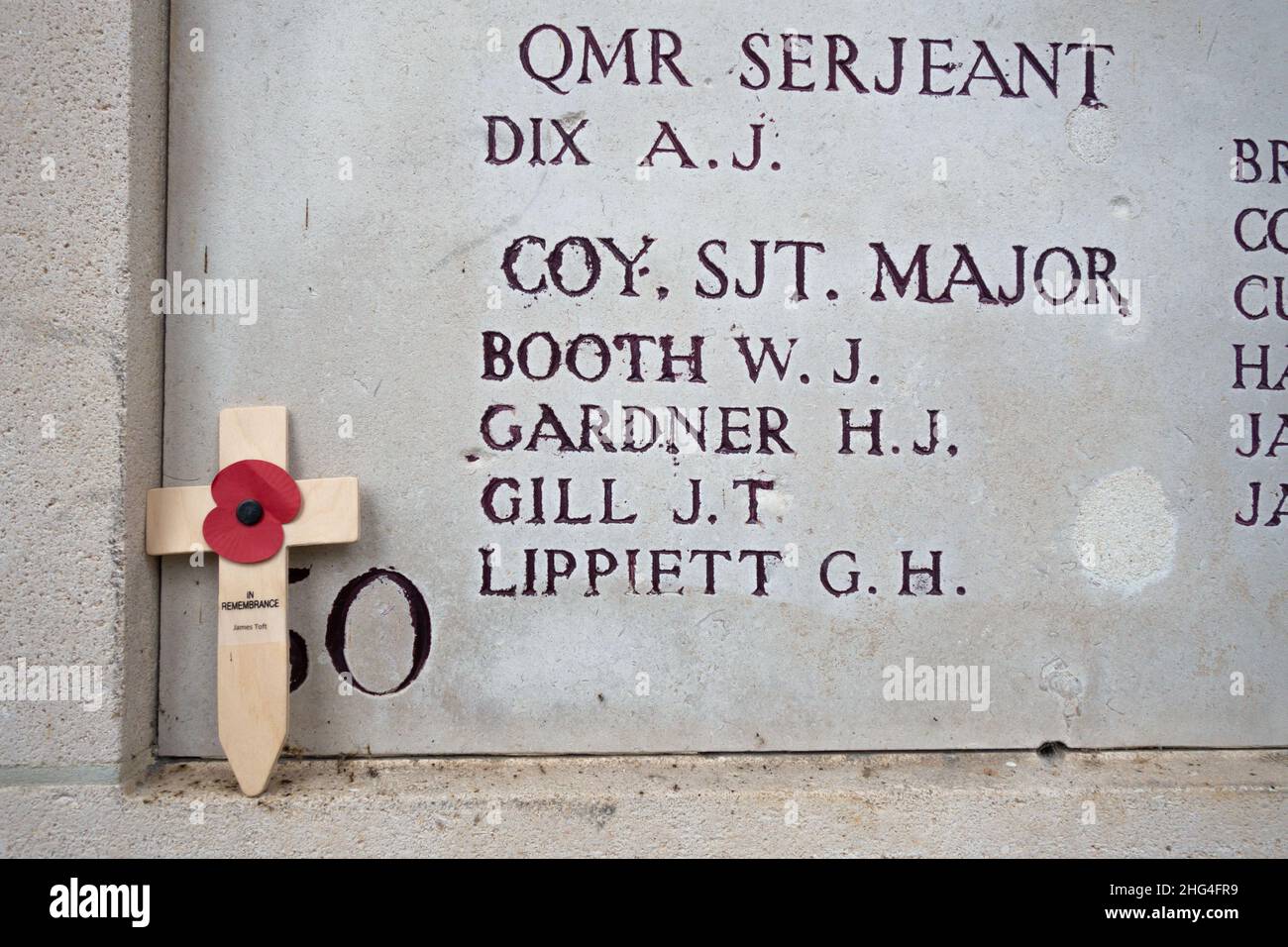 Vor Inschriften mit den Namen gefallener Soldaten steht am Menin Gate in Ypern, Belgien, ein künstlicher Mohnblumen auf einem Kreuz. Stockfoto