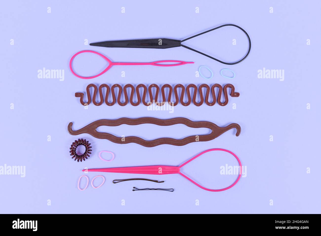 Verschiedene Haarstyling-Werkzeuge wie Bun Maker, Zopf-Werkzeug, Pferdeschwanz-Stil Maker, Haarclip, Gummibänder und Stifte auf violettem Hintergrund Stockfoto