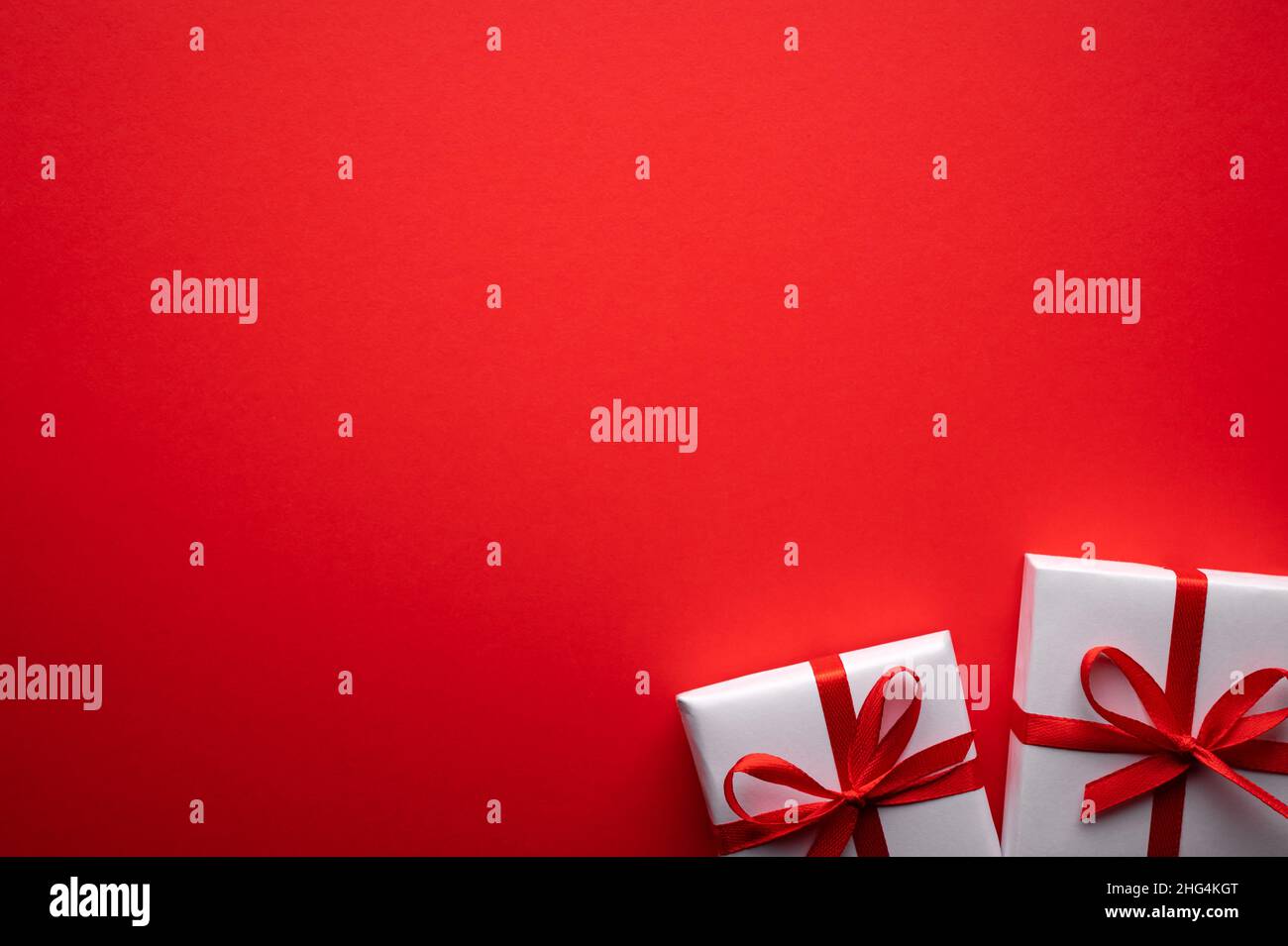 Kreatives Postkarten-Design am Valentinstag mit weißer Geschenkbox und roter Schleife auf rotem Papierhintergrund. Valentinstag und Liebeskonzept Stockfoto