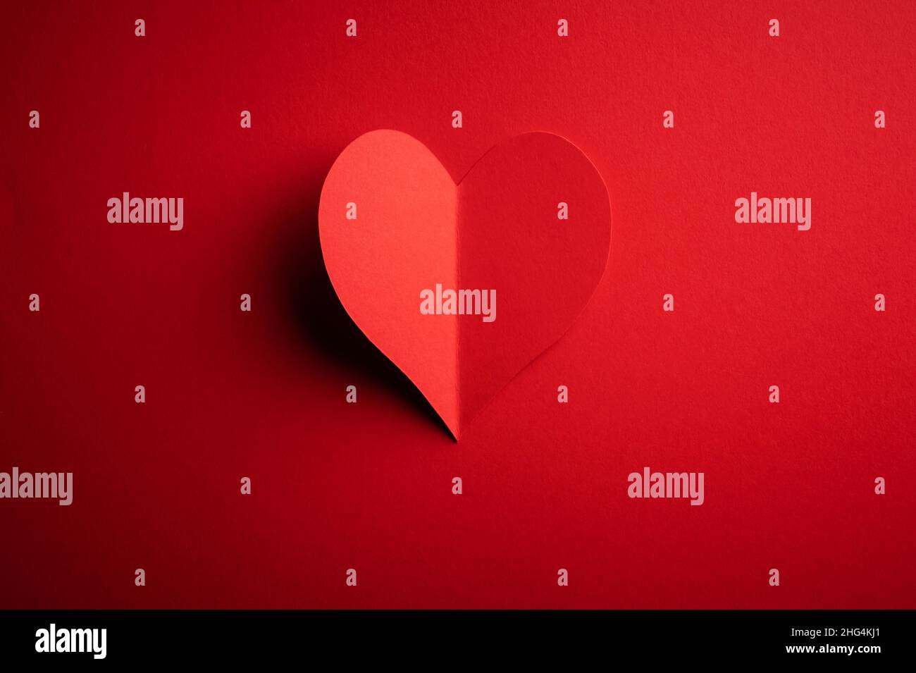 Kreatives Postkarten-Design am Valentinstag mit rotem Papierherz auf rotem Karton-Hintergrund. Valentinstag und Liebeskonzept Stockfoto