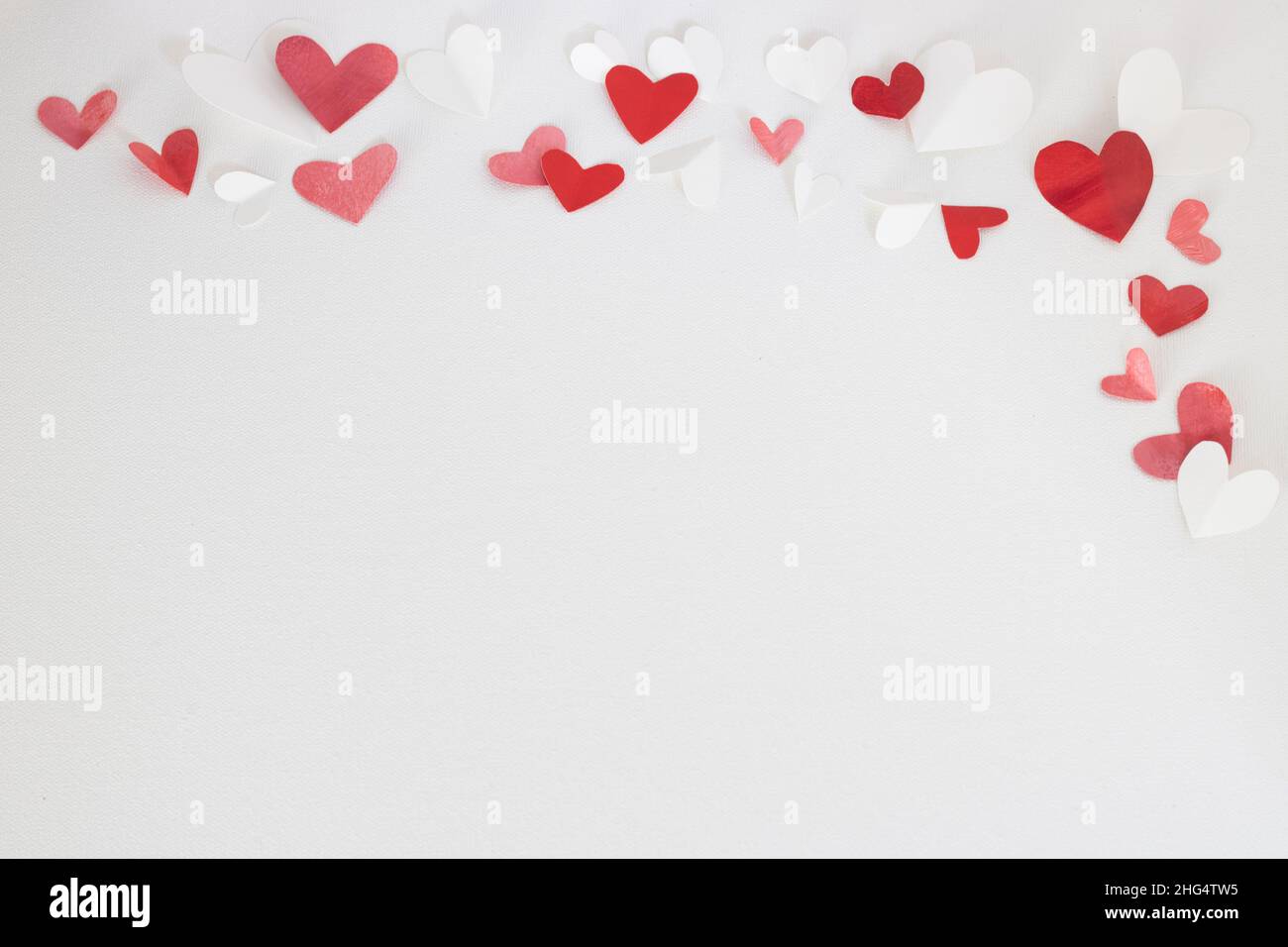 Valentinstag oder Hochzeit, Einladung, verstreut bemalte kleine herausgeschnittene rote, rosa und weiße Herzen mit Kopierraum Stockfoto