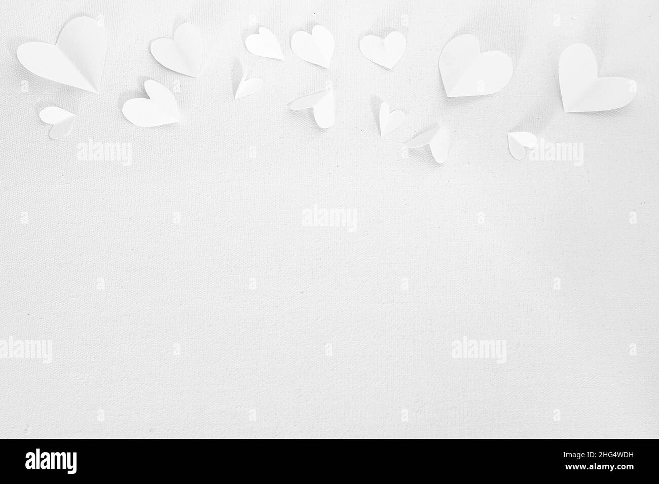 Valentinstag oder Hochzeit, Einladung, kleine ausgeschnittene weiße Herzen auf weißem Leinwandhintergrund, Kopierraum Stockfoto
