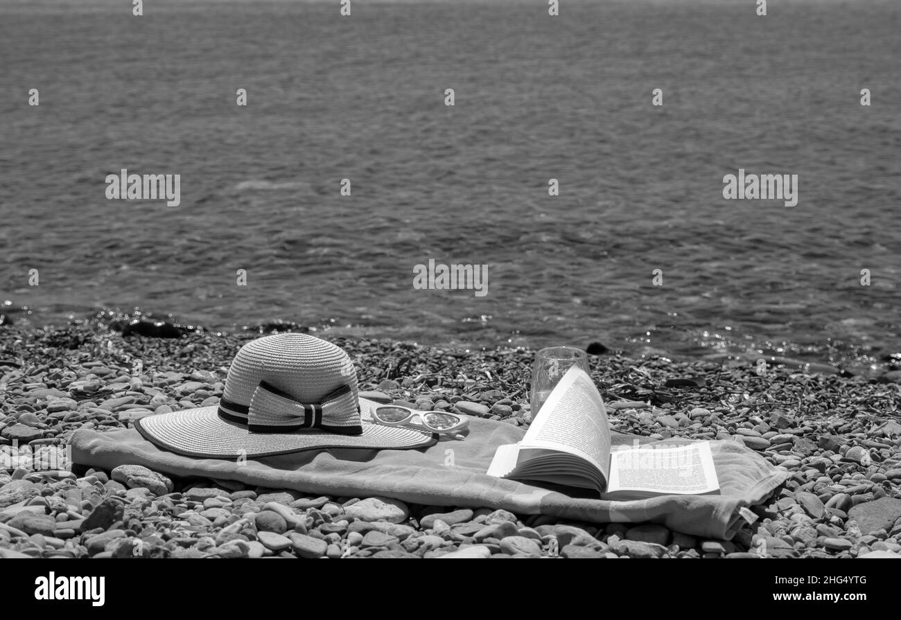 Sommerferienkonzept am Meer mit Handtuch, Hut und Buch, Freizeitaktivitäten am Strand im Urlaub Stockfoto