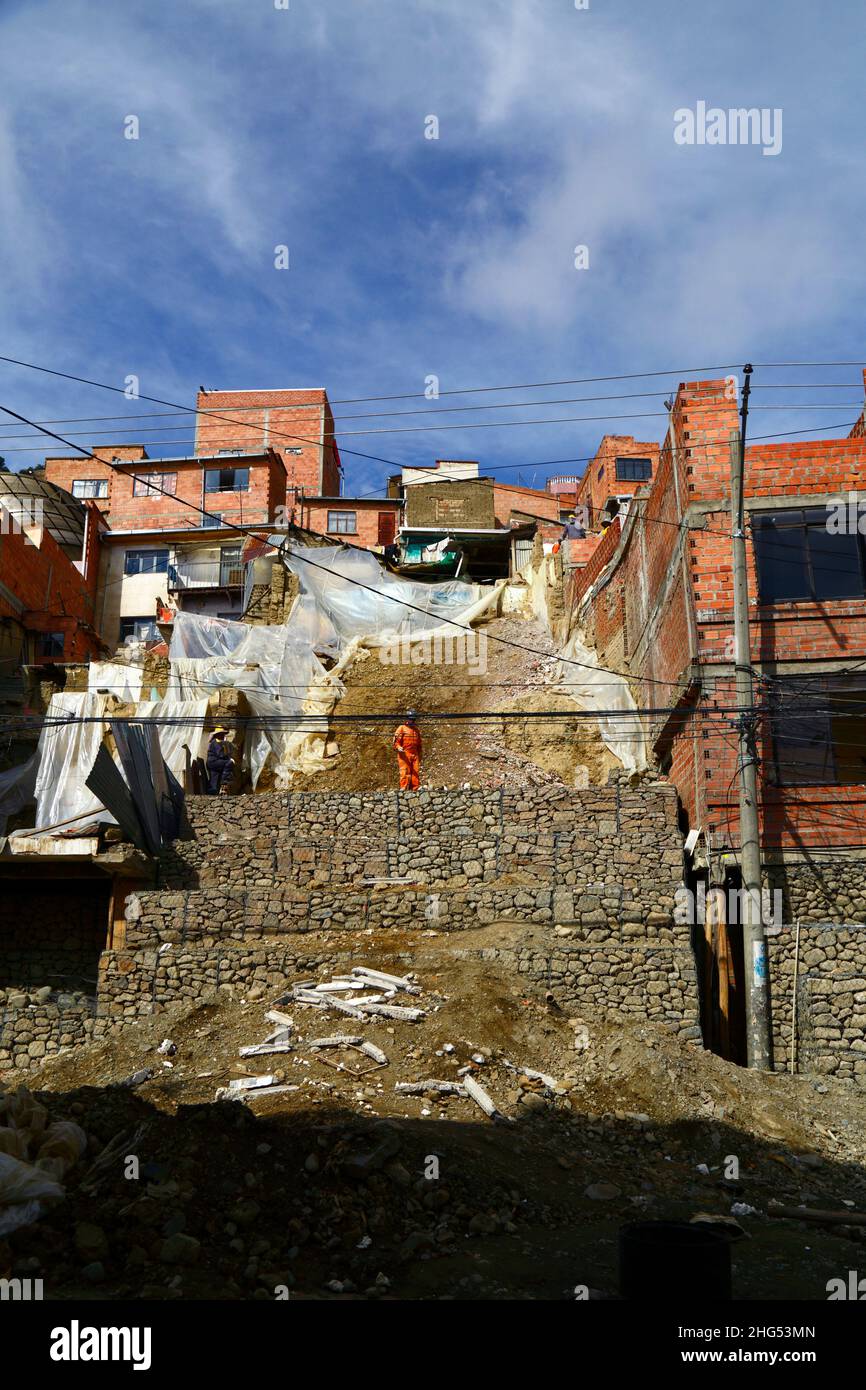 La Paz, Bolivien: Stadtarbeiter, die einen Hügel festbauten und Häuser mit Käfigen mit Steinen/Gabionen an einem Standort in Tembladerani/Cotahuma zerstörten, wo unerlaubte Aushubarbeiten und Erdbewegung einen Teil des Hügels zum Einsturz brachte. Viele der Stadtviertel am Hang von La Paz wurden in instabilen Gebieten ohne entsprechende Genehmigungen oder Gebäudekontrollen errichtet. Absenkungen und Erosionen, die Erdrutsche und Häuser zum Einsturz bringen, sind vor allem in der Regenzeit üblich. Bei diesem Vorfall mussten 2 Häuser abgerissen werden und 6 weitere wurden schwer betroffen. Stockfoto