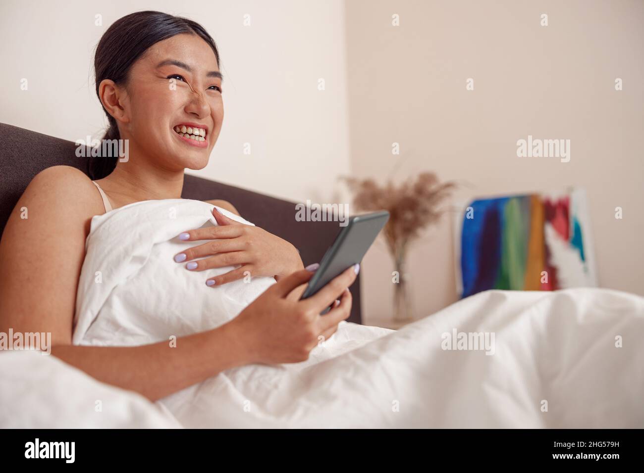 Fröhliche junge Frau mit Smartphone zu Hause Stockfoto