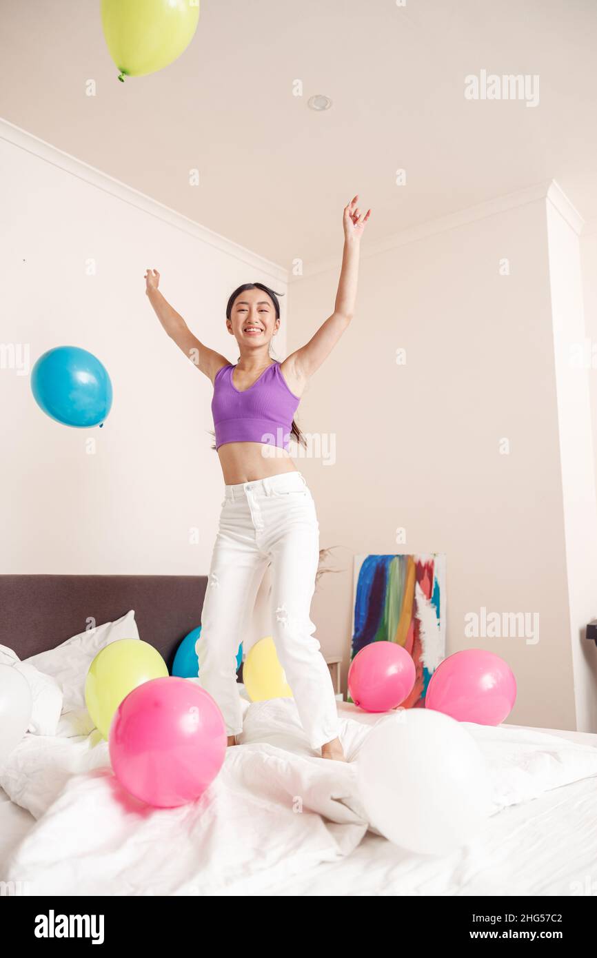 Glückliche junge Frau, die zu Hause mit Luftballons auf das Bett springt Stockfoto