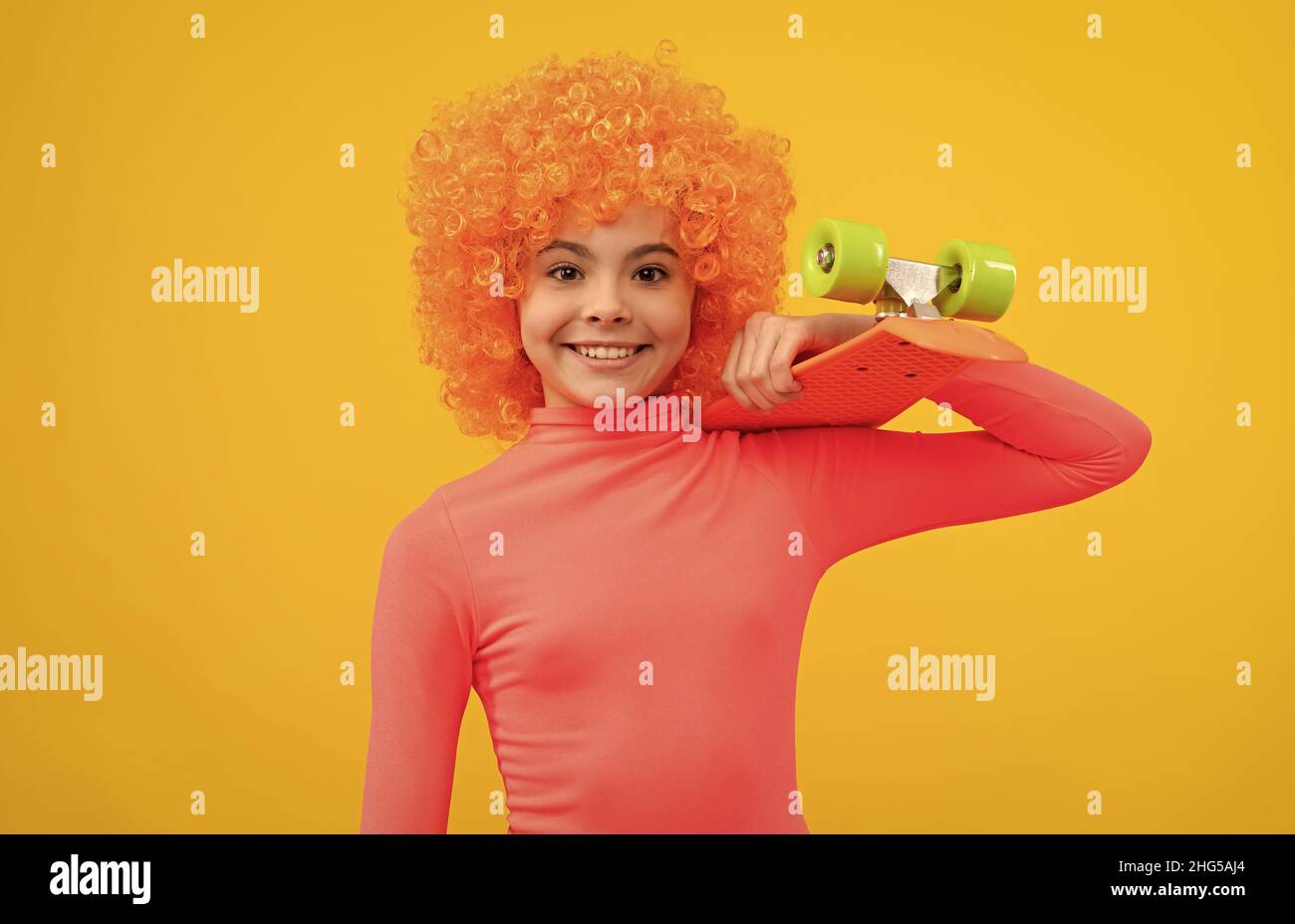 Glückliches Mädchen Kind mit orangefarbenen Haaren in rosa Poloneck Lächeln hält Pennyboard, Pennyboard Stockfoto