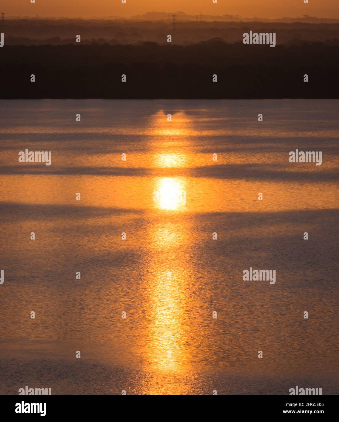 Wunderschöner Hintergrund des Sonnenaufgangs, der sich auf dem Ozean spiegelt, mit immensem Hintergrund von Bäumen und Bergen am Horizont Stockfoto