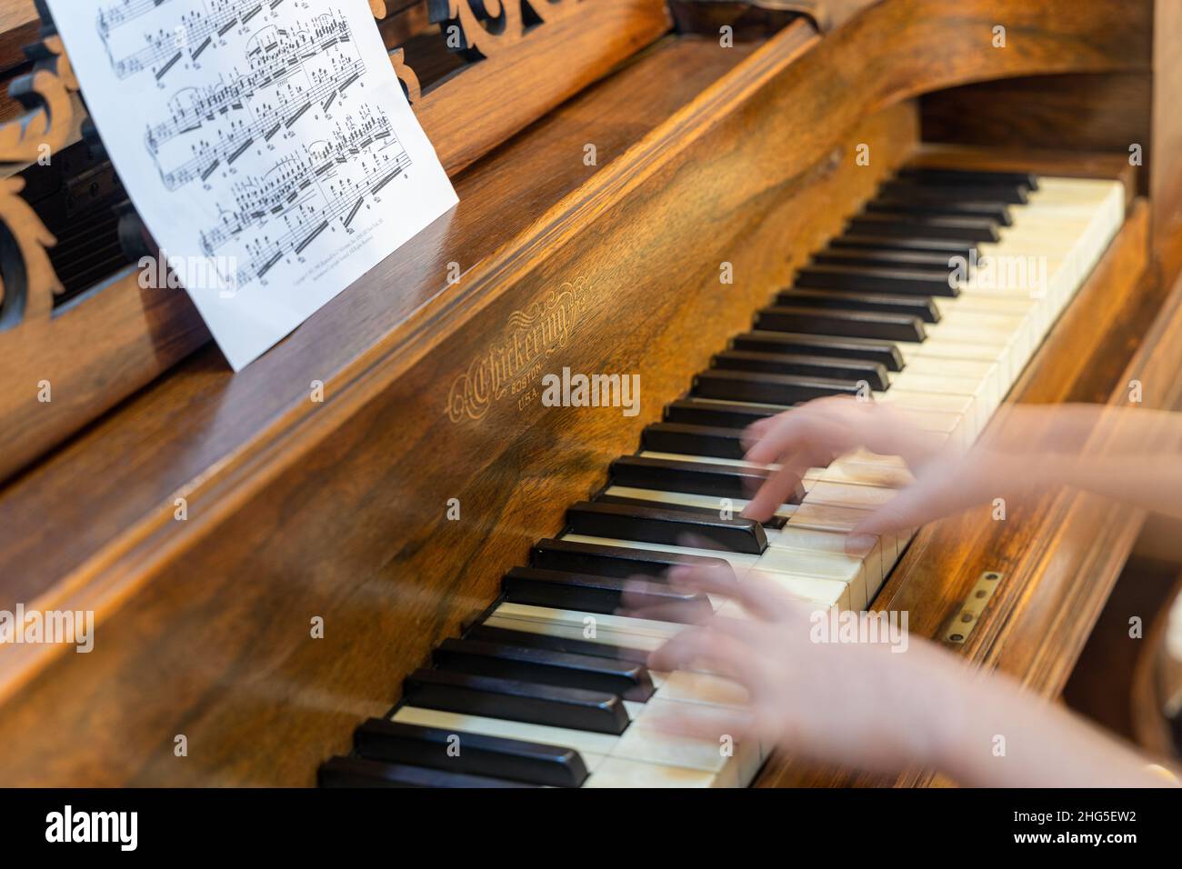 Nahaufnahme eines jungen Mädchens, das ein antikes, seltenes nChickering & Sons Square Grand Klavier spielt, das 1867 mit verschwommenen Händen gebaut wurde. Stockfoto