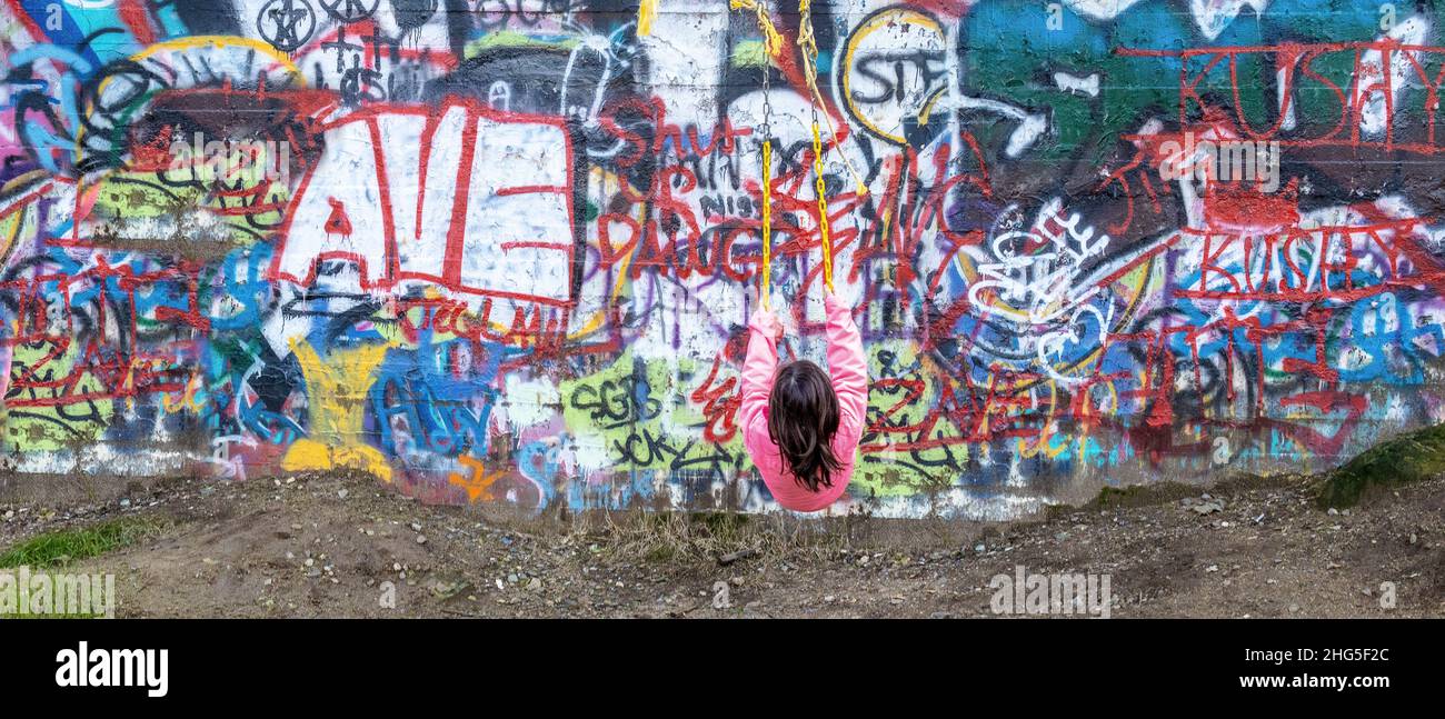 Junge auf einer gelben Schaukel, die vor einer Graffiti-Wand in einer urbanen Umgebung schwingt. Stockfoto