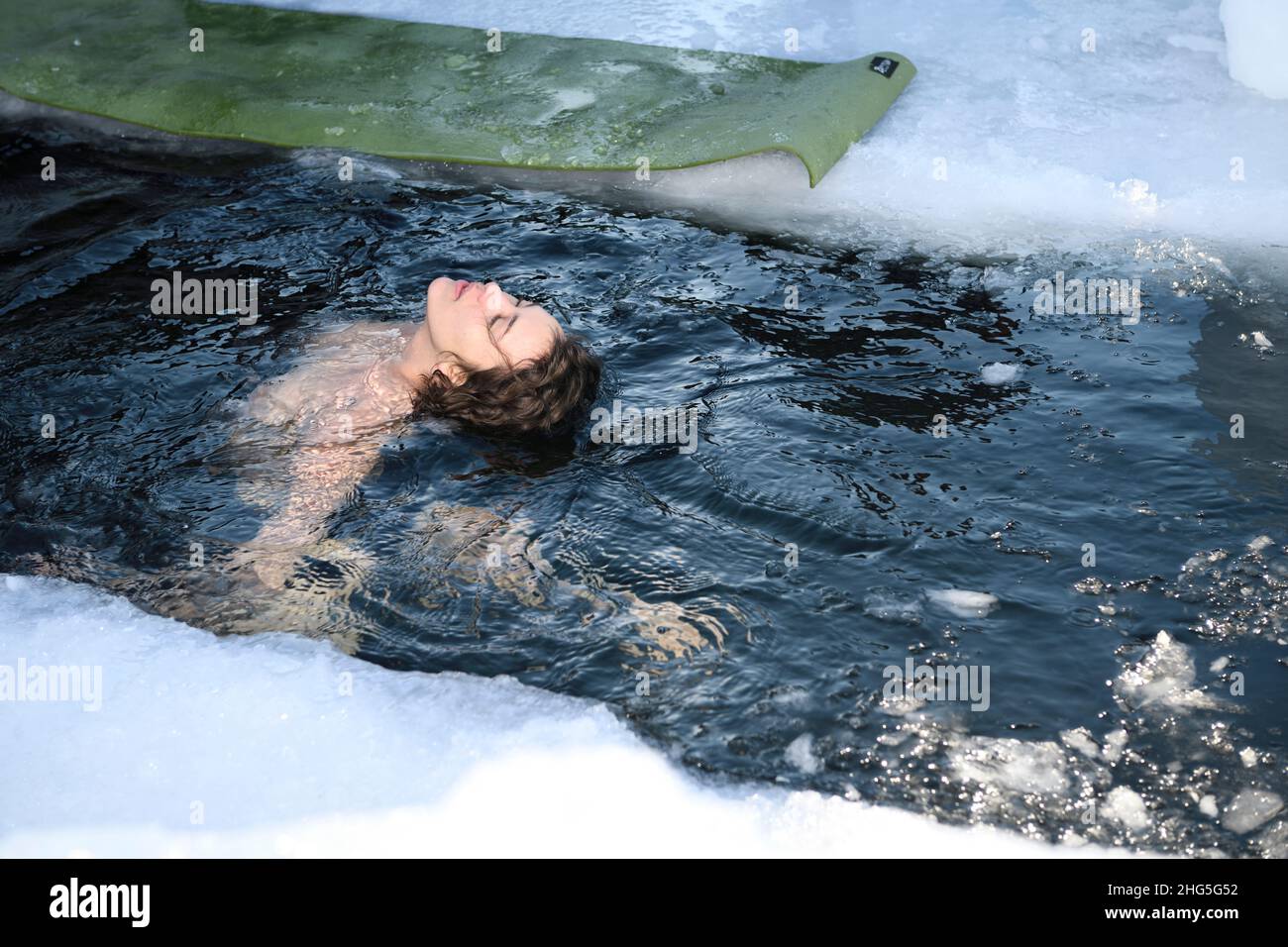 Anmutige junge Frau, die sich während eines kalten Wasserschwimmens im Winter am Kempenfelt Bay Lake Simcoe Barrie Ontario mit dem Kopf ins Eiswasser lehnt Stockfoto