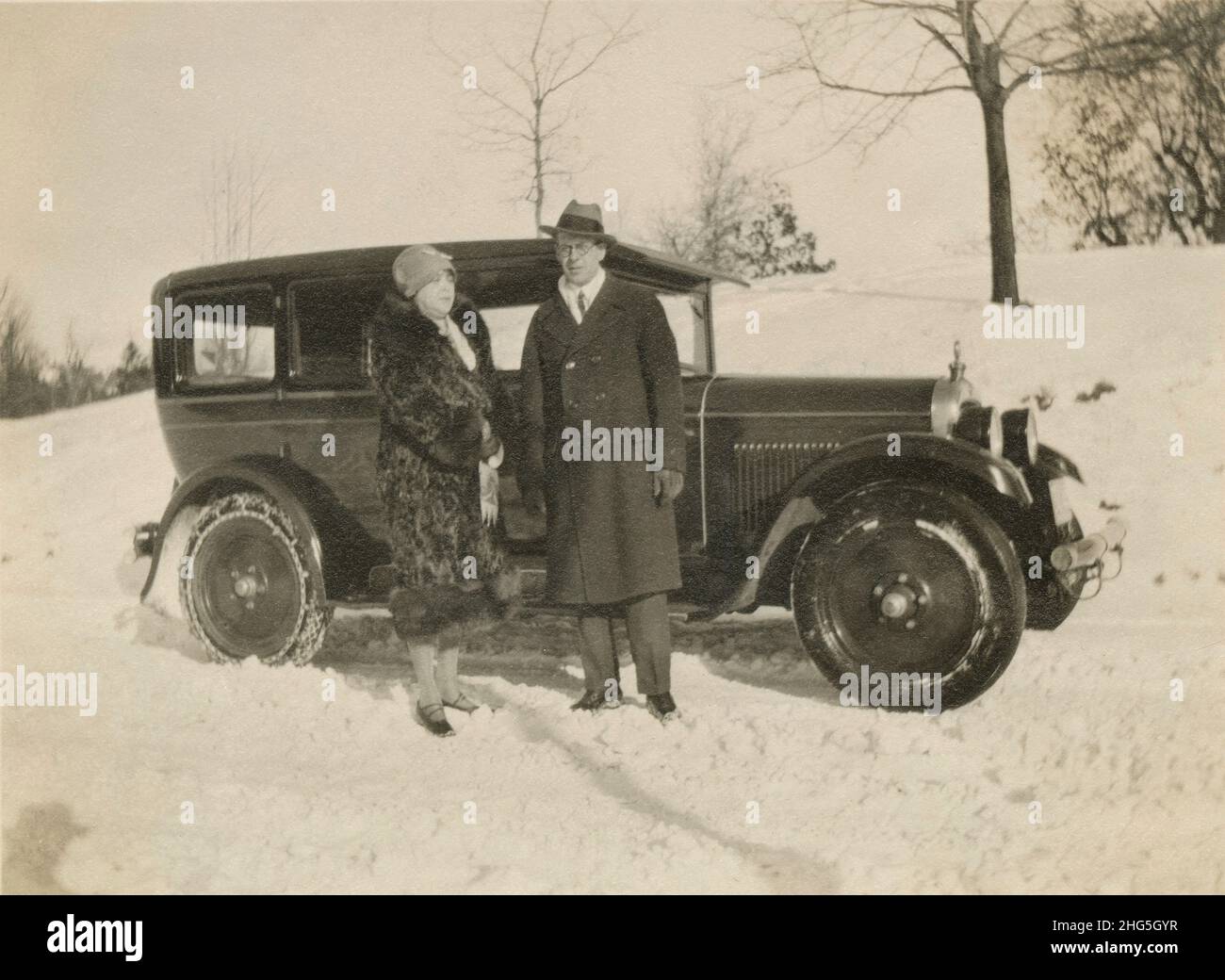 Antike Fotografie um 1920, wohlhabender Mann und Frau in der Nähe des Autos im Schnee. Genaue Lage unbekannt, USA. QUELLE: ORIGINALFOTO Stockfoto